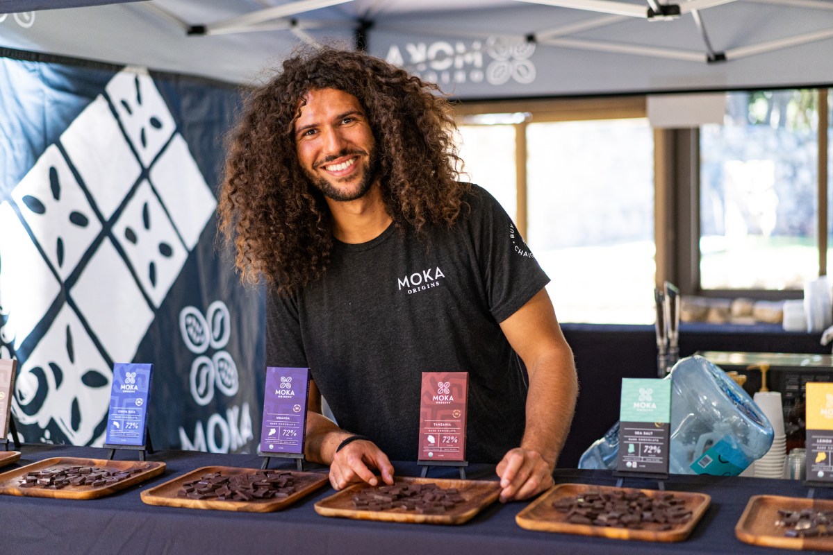 A barista smiles at the camera, on the table are a series of different chocolate bars for people to sample